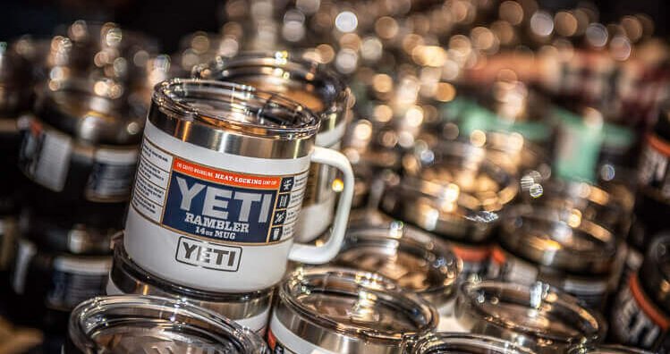 Close-up of a YETI mug on display at an REI store winter event, surrounded by seasonal outdoor gear and festive decorations.